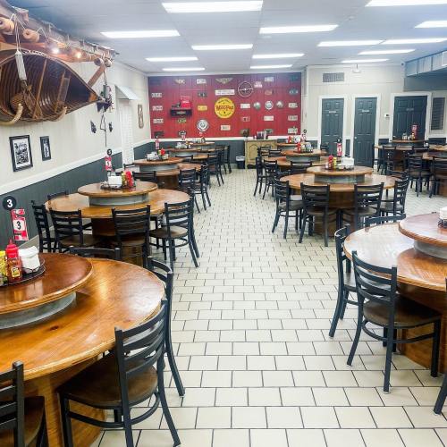 A spacious restaurant interior with wooden tables, black chairs, and red walls adorned with vintage signs.