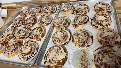 Two trays of freshly baked cinnamon rolls drizzled with icing, arranged neatly on parchment paper.