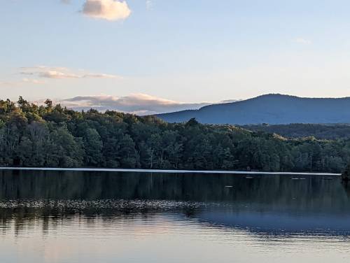 A serene lake surrounded by lush trees and mountains under a clear sky, reflecting the landscape in the water.