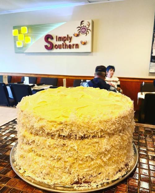 A large coconut cake on a silver platter in a cozy restaurant setting with a sign that reads "Simply Southern."