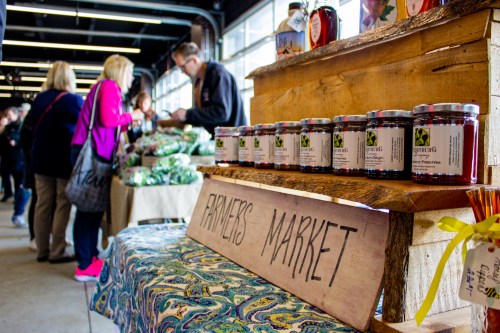 A bustling farmer's market with jars of preserves on display and shoppers browsing fresh produce.