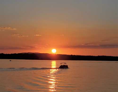 A serene sunset over a calm lake, with a boat leaving a gentle wake in the water.