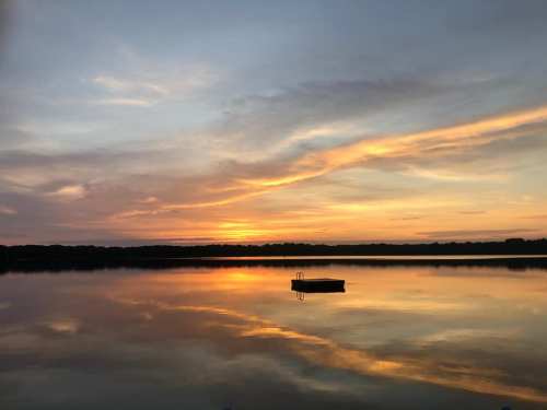 A serene sunset over a calm lake, with vibrant orange and pink hues reflecting on the water's surface.