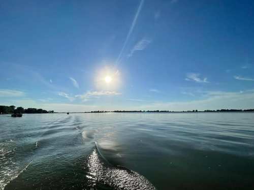 A serene lake scene with gentle waves, under a bright sun and clear blue sky.
