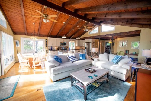 Bright, open living space with a cozy sofa, wooden beams, and a dining area, featuring large windows and natural light.