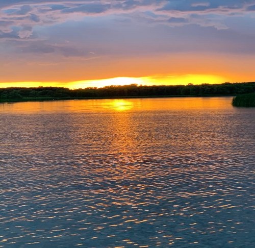 A serene sunset over a calm lake, with vibrant orange and purple hues reflecting on the water's surface.