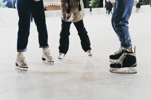 Three pairs of skates on an ice rink, with two adults and a child in the center, ready to skate.