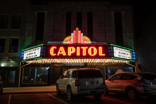 The illuminated Capitol theater marquee at night, featuring colorful lights and a parked SUV in front.