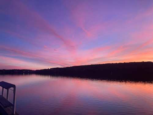 A serene sunset over a calm lake, with vibrant pink and purple hues reflecting on the water's surface.