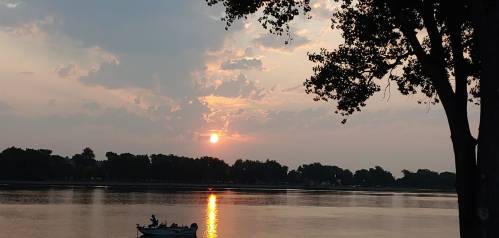 A serene sunset over a lake, with a small boat and silhouetted trees in the foreground.