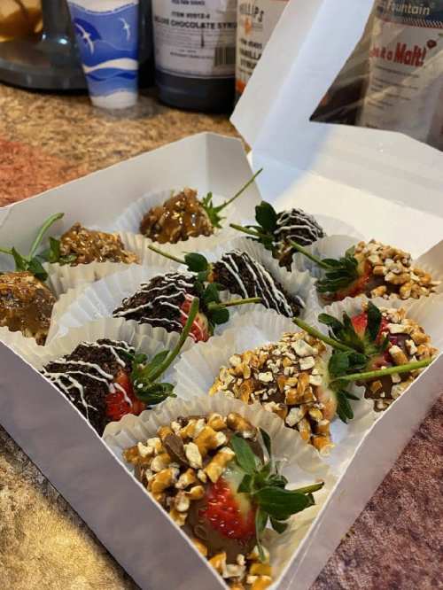 A box of assorted chocolate-covered strawberries, topped with nuts and drizzled with white chocolate.