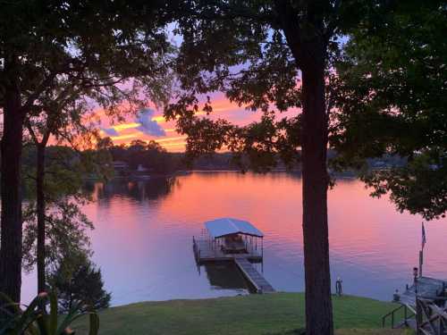 A serene lake at sunset, with vibrant pink and orange skies reflecting on the water and a dock in the foreground.