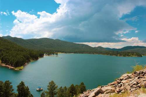 A serene lake surrounded by green mountains and trees under a partly cloudy sky.
