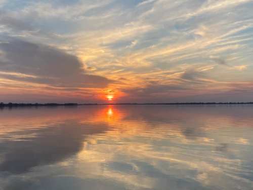 A serene sunset over a calm lake, with vibrant colors reflecting on the water's surface and soft clouds in the sky.