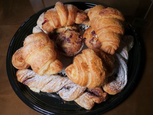 A black platter filled with various pastries, including croissants and muffins, dusted with powdered sugar.