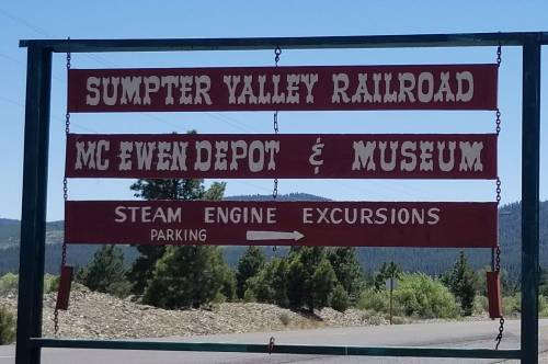 Sign for Sumpter Valley Railroad, McEwen Depot & Museum, indicating steam engine excursions and parking direction.