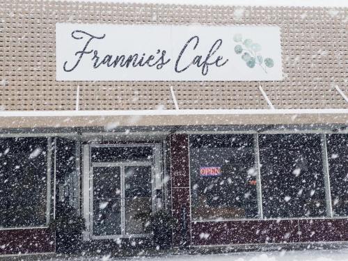 A snowy scene of Frannie's Cafe with an "OPEN" sign in the window, showcasing a cozy atmosphere.