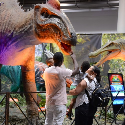A family interacts with a large dinosaur exhibit at a museum, with vibrant colors and detailed features.