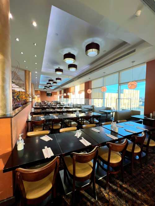 A spacious restaurant interior with rows of tables, elegant lighting, and large windows showcasing a bright view.