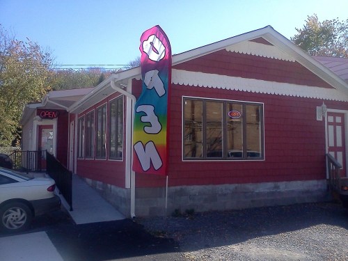A red building with large windows and a colorful "OPEN" flag outside, indicating a welcoming atmosphere.