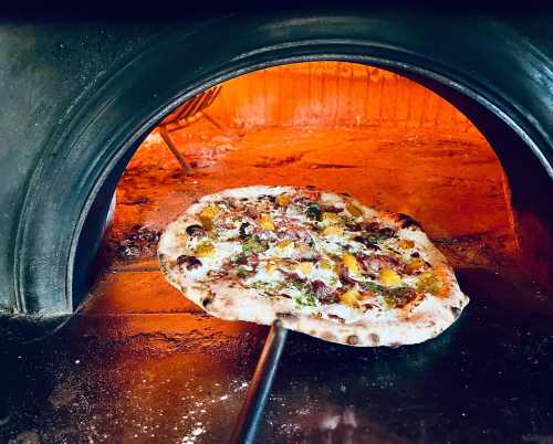 A freshly baked pizza being pulled from a wood-fired oven, with a golden crust and colorful toppings.