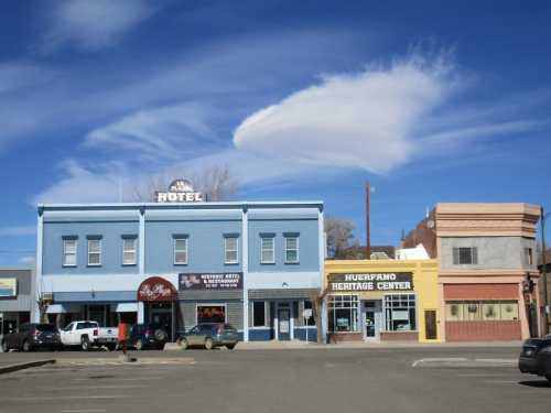 A colorful street scene featuring a blue hotel, heritage center, and unique cloud formation in a clear blue sky.