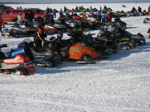 A snowy landscape filled with parked snowmobiles and people enjoying winter activities.