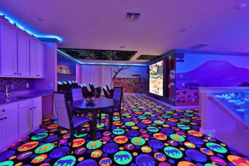 A vibrant room with a colorful, glowing animal-patterned floor and illuminated walls, featuring a dining area and kitchen.