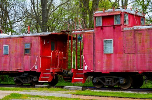 Two vintage red cabooses parked side by side, surrounded by greenery and trees.