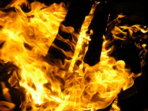 Bright flames engulfing logs, creating a dynamic display of orange and yellow fire against a dark background.