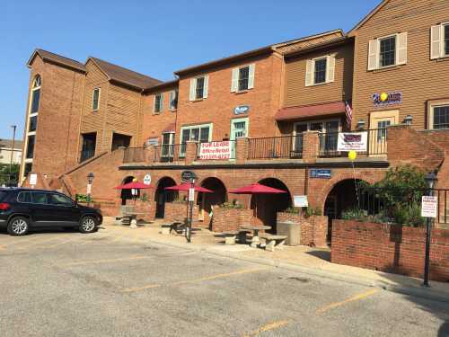 A brick building with multiple levels, featuring storefronts and outdoor seating, under a clear blue sky.