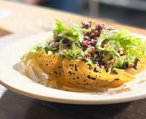 A vibrant salad served in a crispy cheese bowl, topped with greens, nuts, and pomegranate seeds.