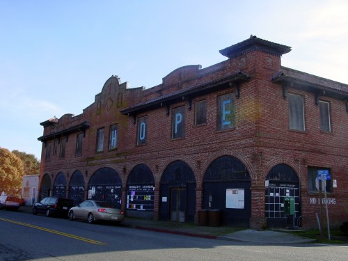 Abandoned brick building with "HOPE" painted on the front, featuring arched windows and a vintage aesthetic.