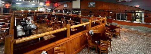 A spacious restaurant interior with wooden booths, tables, and a buffet area, featuring warm lighting and rustic decor.
