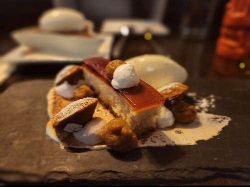 A slice of cake topped with caramel, cream, and nuts, served on a dark slate plate.