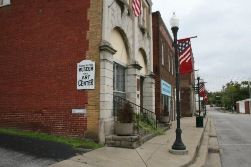 Exterior view of a museum and art center with American flags, set on a quiet street lined with brick buildings.
