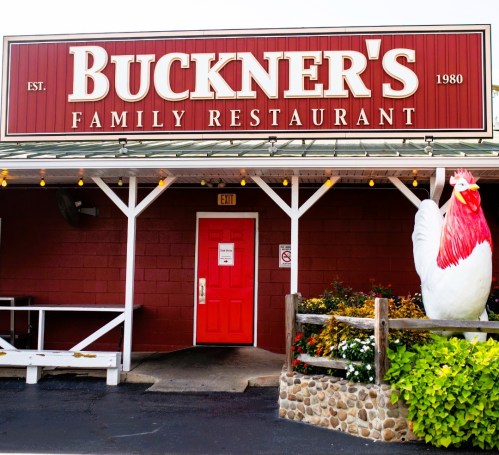 Exterior of Buckner's Family Restaurant, featuring a red sign, a bright red door, and a large chicken statue.