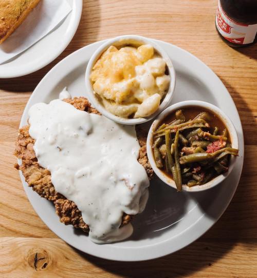A plate featuring fried chicken smothered in white gravy, macaroni and cheese, and green beans on the side.