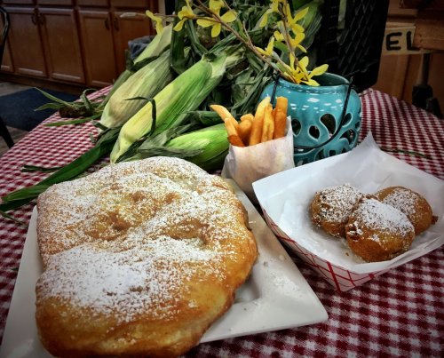 A plate of fried dough dusted with powdered sugar, alongside corn, fries, and a blue decorative cup.