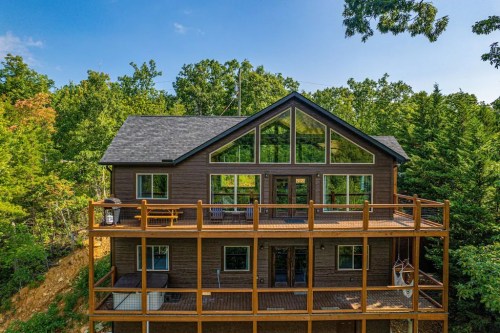 A modern two-story cabin with large windows, surrounded by trees and featuring a spacious deck.