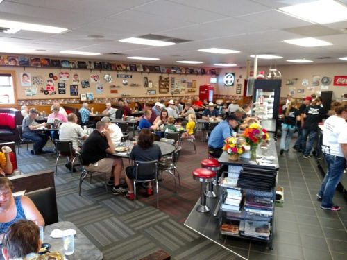A busy diner filled with people eating and chatting, decorated with vintage signs and memorabilia on the walls.