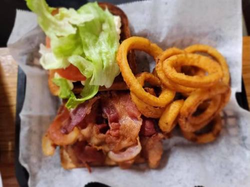A close-up of a sandwich with bacon, lettuce, and tomato, served with curly fries on the side.