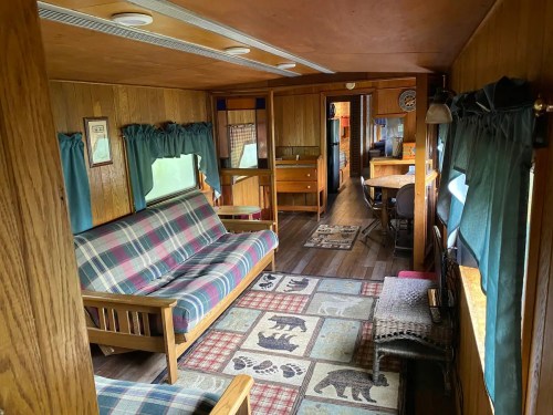 Cozy interior of a rustic cabin with wooden walls, a plaid sofa, and a patterned rug featuring bears.