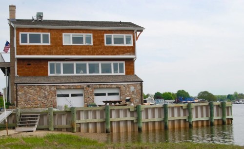 A two-story house with wooden siding and stone accents, located by a calm waterway with a dock.