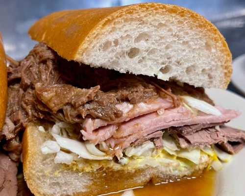 Close-up of a hearty sandwich filled with layers of roast beef, ham, and shredded cabbage on a soft bun.