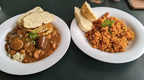A plate of gumbo with sausage and bread, alongside a plate of jollof rice garnished with green herbs.