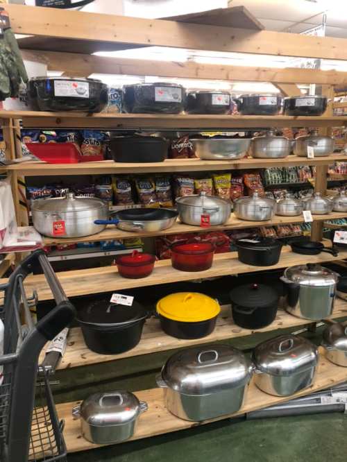 A display of various pots and pans on wooden shelves, with colorful lids and packaging in the background.