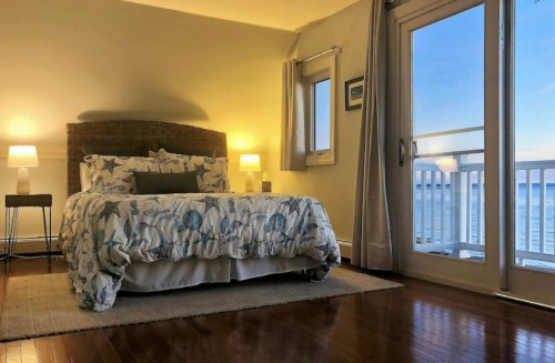 Cozy bedroom with a floral bedspread, two lamps, and a view of the ocean through sliding glass doors.