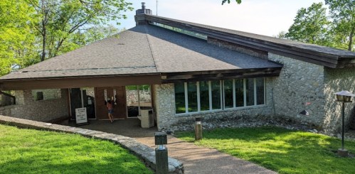 A modern stone building with large windows, surrounded by greenery and a pathway leading to the entrance.