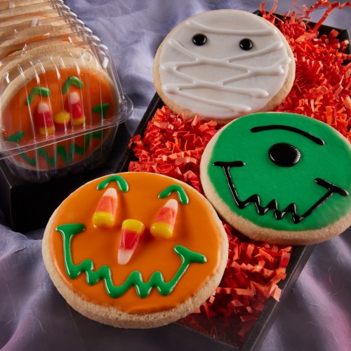 Colorful Halloween-themed cookies featuring a pumpkin, mummy, and monster designs on a bed of orange filler.